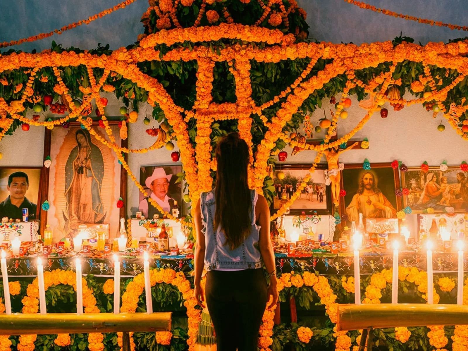 Visitante frente a un altar de Xantolo con arco de cempasúchil, veladoras y retratos de los difuntos, en la Huasteca Potosina
