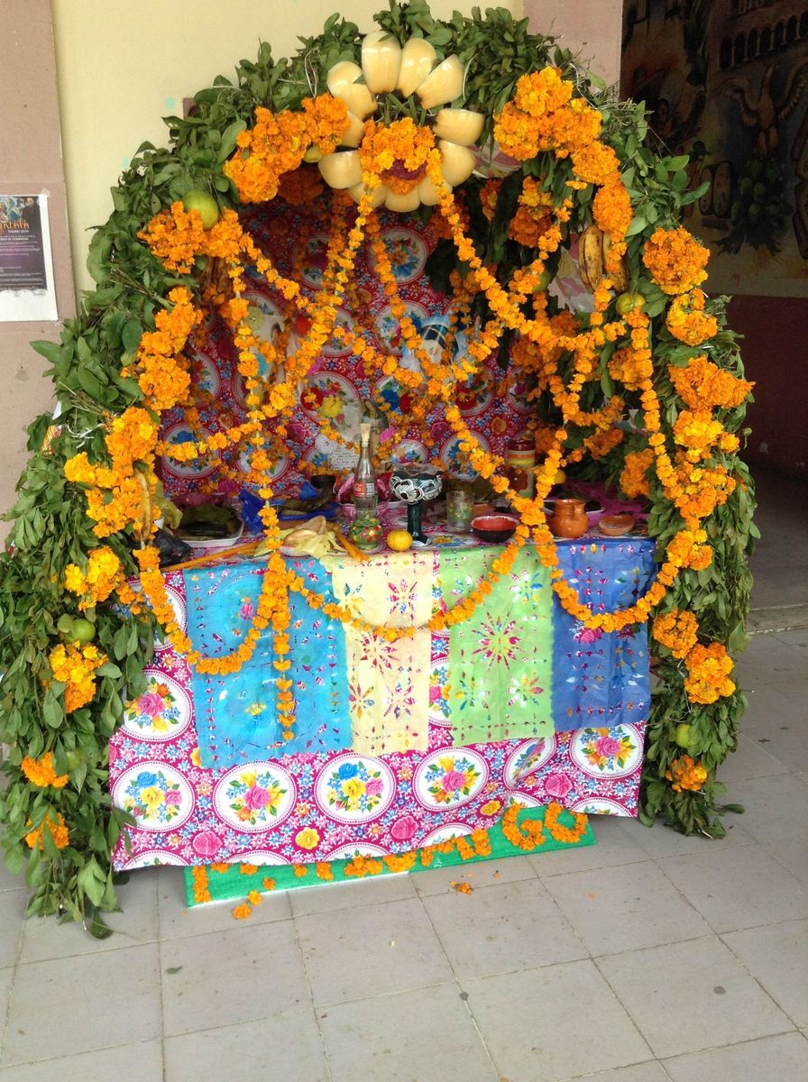 Altar de Xantolo bajo un arco de palmilla y flor de cempasúchil, con manteles de colores
